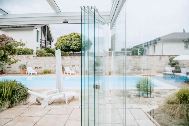 Geöffnete COVER Schiebe-Drehverglasung mit zusammengeschobenen Glasflügeln vor einem Pool