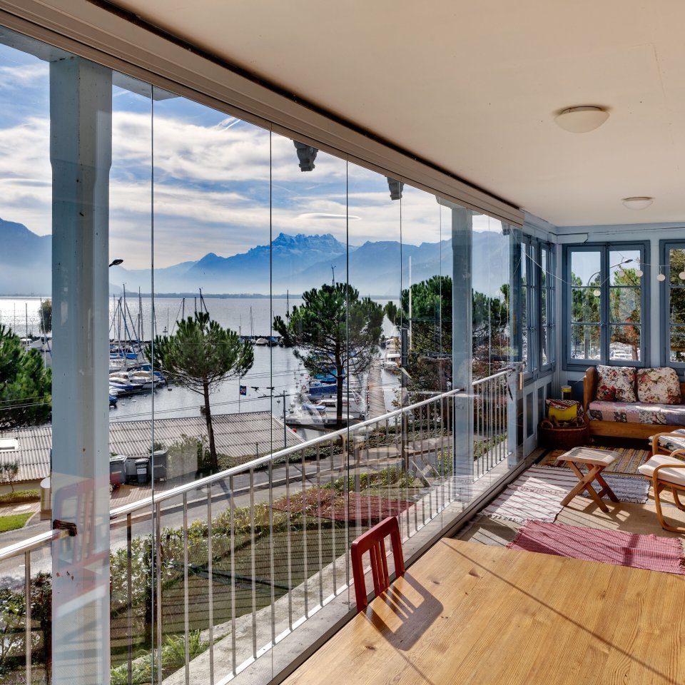 Verglaste Terrasse mit COVER Schiebe-Drehverglasung und Blick auf Hafen, See und Berge