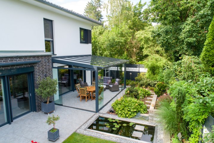Anthrazitfarbene Veranda mit Glasdach und Schiebeverglasung SLIDER, davor ein Garten mit Seerosenteich